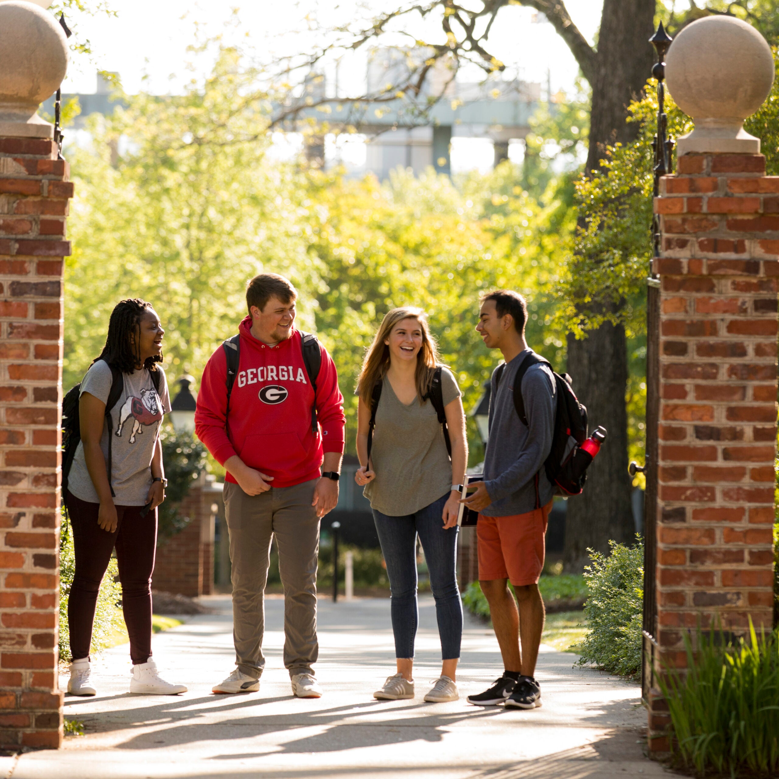 Four University of Georgia students chatting and smiling as they walk through a brick campus gateway.